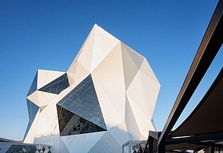 Futuristisches Gebäude der Sky-Venture-Anlage auf Yas Island mit weißer Fassade und großen Glasflächen, gespiegelt in einer Wasserfläche im Vordergrund