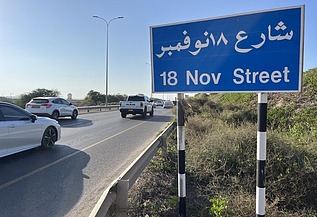 Straßenschild der 18 November Street an einer mehrspurigen Straße mit Fahrzeugverkehr, Leitplanken und begleitender Verkehrsinfrastruktur.ehr