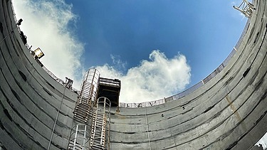 Blick aus einem tiefen Betonschacht auf Himmel, Steigleitern und eine Hebebühne beim Bau der Verbindungskanäle des DTSS
