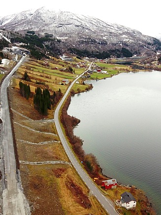 A lake, next to it a road, snowy mountains in the distance