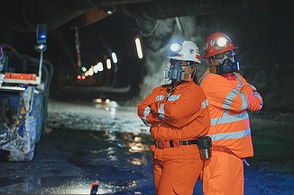 Personnel wearing protective equipment inside an underground tunnel at El Teniente Mine in Chile, with tunnel infrastructure and mining facilities visible in the background.