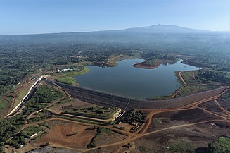 Luftbild einer Damm- und Speicheranlage mit Wasserreservoir, Dammkörper und zugehöriger Infrastruktur in weitläufigem Gelände.