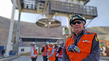 Mining site at the Chuquicamata Underground Mine Development project, showing a shaft hoisting structure, personnel in safety gear, and mine infrastructure in the background