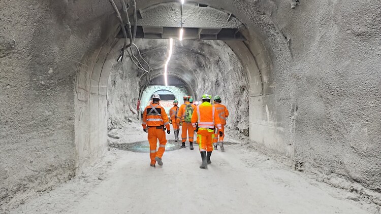 Miners in orange protective clothing walking through an illuminated tunnel in the Chuquicamata Underground Mine North