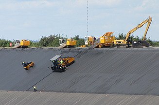 Mehrere Baumaschinen auf einer geneigten Böschung zur Herstellung oder Sicherung einer technischen Oberflächenabdichtung. 