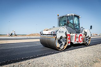 Road roller compacting a newly laid asphalt surface during road construction works.