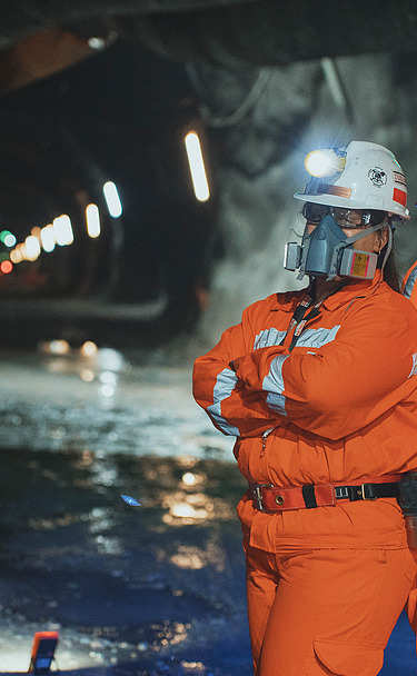 Personnel wearing protective equipment inside an underground tunnel at El Teniente Mine in Chile, with tunnel infrastructure and mining facilities visible in the background.