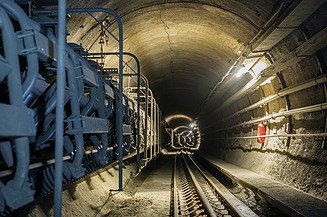 Innenansicht eines Eisenbahntunnels mit Gleisen, Kabelanlagen, technischer Ausrüstung und ausgebauter Tunnelröhre.
