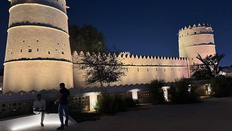 Beleuchtete Gebäude des Al Ain Museums in Abu Dhabi mit traditionellen Türmen und Ummauerung in den Abendstunden.