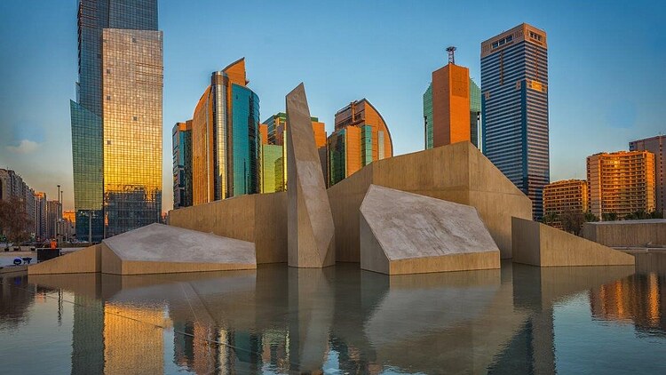 Skulpturales Betonbauwerk des Cultural Foundation Building in Abu Dhabi, umgeben von einem Wasserbecken und modernen Hochhäusern im Hintergrund.
